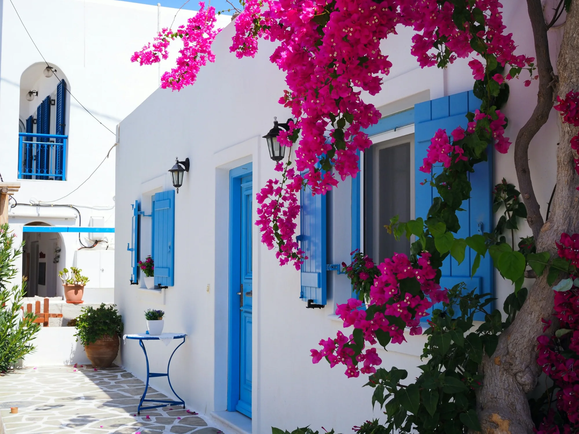 White Greek island house with blue shutters and bougainvillea